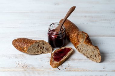 Beyaz ahşap masada ahududu reçeli dilimlenmiş çoklu tahıllı baget. Tatlı yemek.