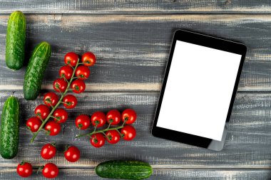 Çeri domatesleri, salatalıklar ve tablet bilgisayarı siyah masanın üstünde. Sebze. Tarif salatası, vejetaryen menüsü.