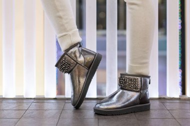 İç taraftaki modelin bacaklarında yapay elmaslar olan güzel gümüş ugg dişileri. Yan görüş. Ayakkabı mağazası. Şenlikli ayakkabılar.
