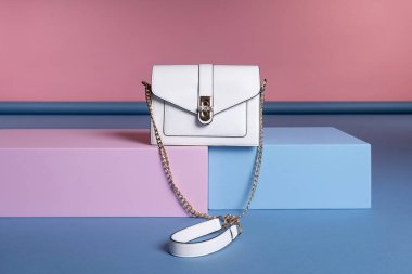 Küçük bir kadın dikdörtgen çantasının zincir kayışı üzerinde pembe, mavi bir standın üzerinde duruyor. Stüdyo fotoğrafı