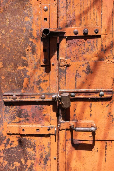 old closed metal gates. Lots of locks on the closed door. Bolts on metal gates. Old Ginger metal gates. Old padlock on the door.