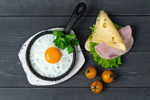 breakfast of fried egg and toast with cheese, ham, lettuce and cherry tomatoes on black wooden table. Light breakfast