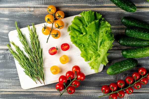 rosemary, leaves lettuce, cucumbers and branch cherry tomatoes on white cutting board. set vegetables for salad