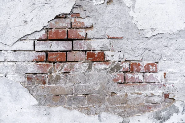 brick wall background with white fallen off plaster. The brick wall is visible from under the white plaster. White stucco and brick wall texture. piece of brick wall under plaster