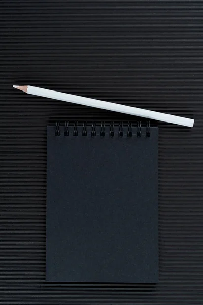 Cuaderno negro y lápiz blanco sobre fondo de cartón ondulado negro. Mock Up Notepad of black paper and white pencil lie on corrugated cardboard background. Copie el espacio.. — Foto de Stock