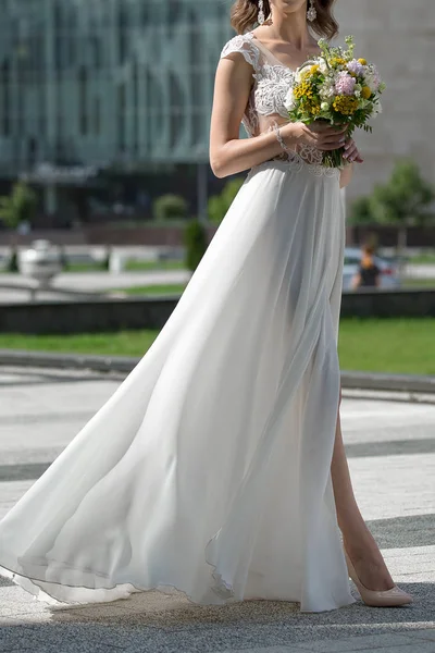 light airy wedding dress with a slit for the legs. The bride walks in a simple elegant wedding dress. White dress with a high slit flutters in the wind during a walk.