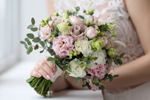 新娘手里拿着一束婚纱 背景是一件白色的婚纱 婚礼当天的新娘花束 送给新娘的花 一个小新娘的花束特写 图库照片