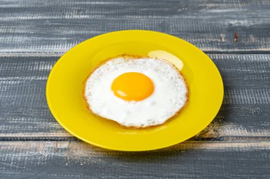 Siyah ahşap masada, sarı tabakta kızarmış yumurta.