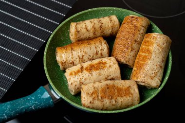 Doldurulmuş krep pişirmek. İştah açıcı krepler yeşil bir tavada ısıtılır..