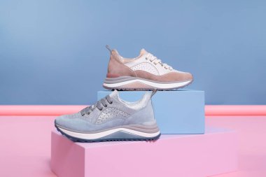 Farklı renklerde ama aynı modelden olan kadın ayakkabıları stüdyodan gelen pembe, mavi bir standın üzerinde duruyor. Tanıtım fotoğrafı.