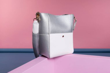 Omuz askısı olan beyaz ve gri, dikdörtgen bir çanta pembe, mavi bir standın üzerinde ilginç bir şekilde duruyor. Stüdyo fotoğrafı