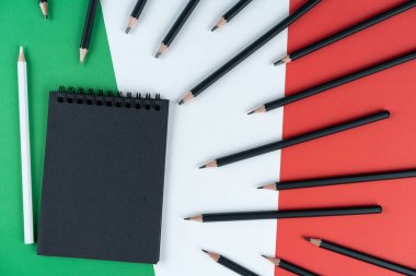 Kara Liste İtalya. Siyah defter, bir sürü siyah kalem ve bir beyaz kalem İtalyan bayrağında yatıyor. Model oluştur, boşluğu, deseni, karton dokuyu kopyala.