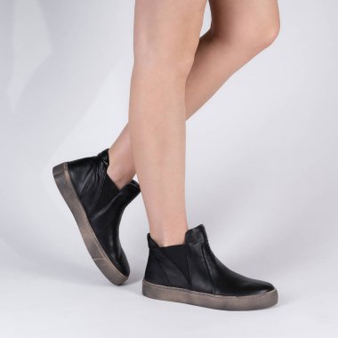 Kadınlar için klasik deri yüksek spor ayakkabılar. Beyaz arka planda bir modelin bacaklarındaki fotoğraf