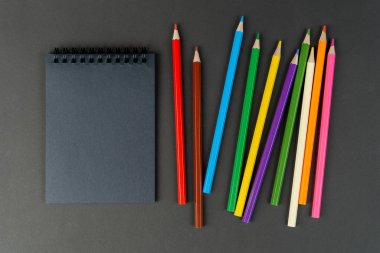 Siyah arka planda siyah defter ve renkli kalemler. Siyah kağıtların ve renkli kalemlerin Mock Up Defteri kağıt arkaplanda. Boşluğu kopyala.