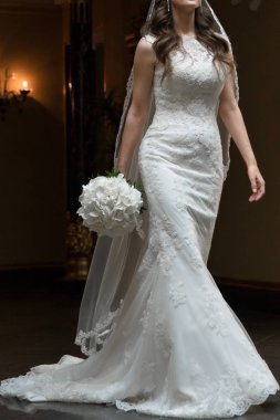Chic white wedding dress silhouette with long beautiful train. Veil on the head of bride. The bride is posing cool in wedding dress. wedding bouquet of white flowers