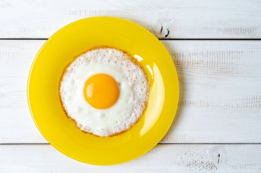 Sarı tabakta kızarmış yumurta ve beyaz ahşap masa. en üstteki görünüm