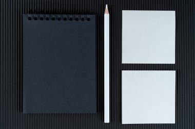 Siyah defter, kalem ve iki beyaz notla siyah burgulu karton arka plan. Model Yukarı. Boşluğu kopyala.