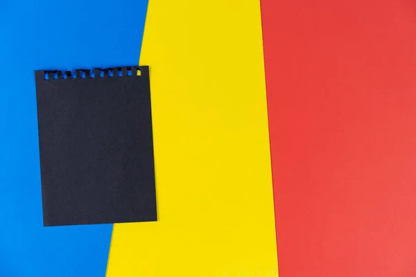 Black list Romania. Mourning, ban, sanctions, politics. black sheet of notebook lies on Romanian flag. Mock up, copy space, pattern, cardboard texture.