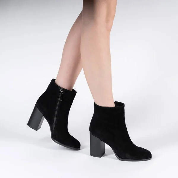 black leather female high-heeled ankle boots on model legs shooting in studio on a white background