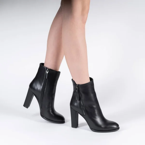 black leather female high-heeled ankle boots on model legs shooting in studio on a white background