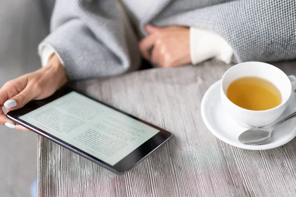 girl reading e-book in cafe. On table is cup of tea and electronic book. tablet on table in cafe, girl reads and drinks tea.