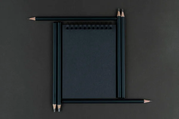 black notebook in frame from black pencils. Mourning, dark, gloomy. Stationery set.