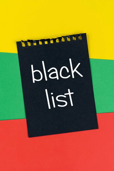 Black list Lithuania. Mourning, ban, sanctions. black sheet of notepad is on Lithuanian flag. Mock up, copy space, pattern, cardboard texture.