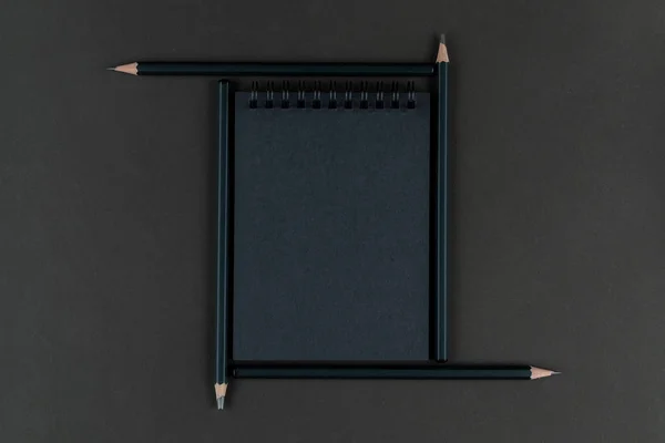 black notebook in frame from black pencils. Mourning, dark, gloomy. Stationery set.