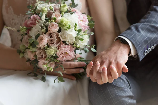 Жених и невеста держат свадебный букет. Руки молодоженов и свадебный букет. Свадебный букет в руках молодоженов. Невеста и жених руки рядом и держать цветы . Лицензионные Стоковые Фото
