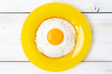 Sarı tabakta kızarmış yumurta ve beyaz ahşap masa. en üstteki görünüm