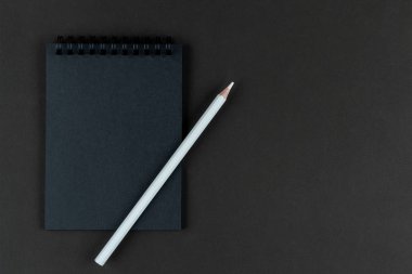 Siyah arka planda siyah defter ve beyaz kalem. Kağıt arkaplanda duran siyah kağıt ve beyaz kalemi taklit et. Boşluğu kopyala.