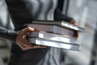 Kız kitapçıda birkaç büyük kitap tutuyor.
