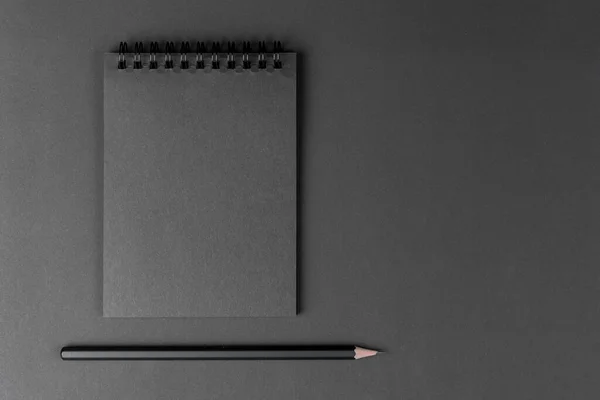 Cuaderno negro y lápiz sobre fondo negro. Mock Up Bloc de notas de papel negro y lápiz negro acostado sobre el fondo de papel. Copiar espacio . —  Fotos de Stock