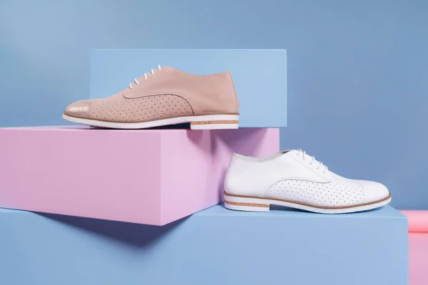 Farklı renklerde kadın ayakkabıları, ama aynı modelden, stüdyodan pembe, mavi bir standın üzerinde duruyor. Tanıtım fotoğrafı.