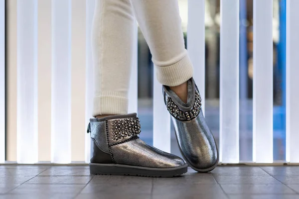 İç taraftaki modelin bacaklarında yapay elmaslar olan güzel gümüş ugg dişileri. Yan görüş. Ayakkabı mağazası. Şenlikli ayakkabılar.