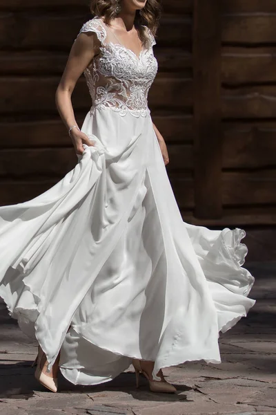 wedding dress with a long slit for legs and lace top. The bride walks in the park in a beautiful white dress. The wedding dress flutters in the wind while walking through the park.