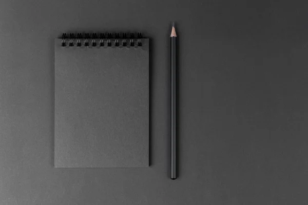 black notebook and pencil on black background. Mock Up Notepad of black paper and black pencil lying on paper background. Copy space.