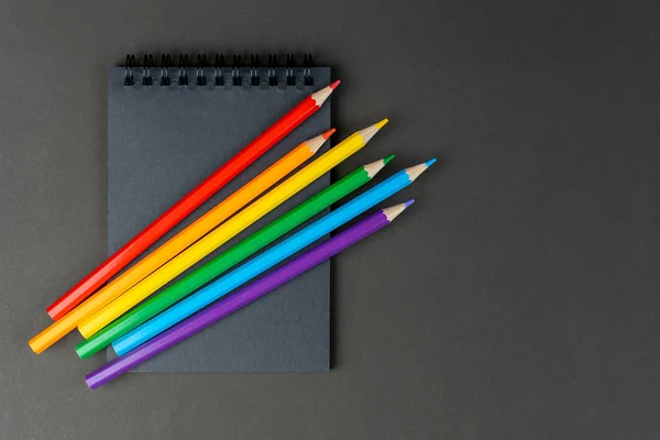 Siyah arka planda siyah defter ve lgbt renkli kalemler. Siyah kâğıt ve lgbt renkli kalemlerden oluşan Mock Up Defteri kağıt arkaplanda yatıyor. Boşluğu kopyala.