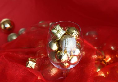 Altın ve kırmızı Noel arkaplanı, içinde şarap kadehi ve altın noel süslemeleri var. Noel süslemeleri ile sarmaşık camı