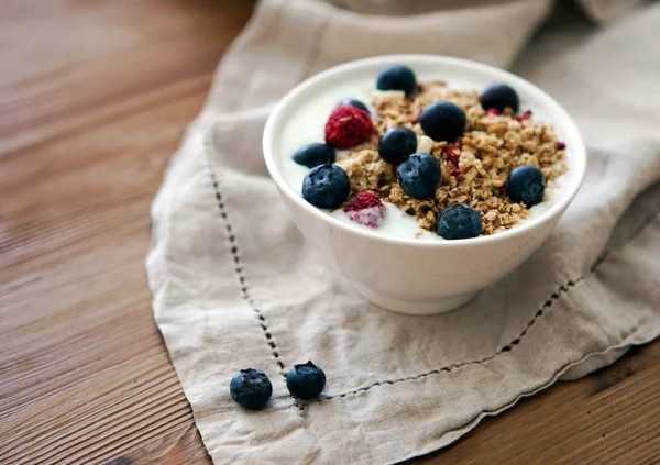 Delicious yogurt breakfast bowl with muesli and fresh blackberries on a wooden table and linen kitchen-towel. Healthy and organic nutrition concept. Blackberry and raspberry muesli. Yogurt in a bowl — Stock Photo, Image
