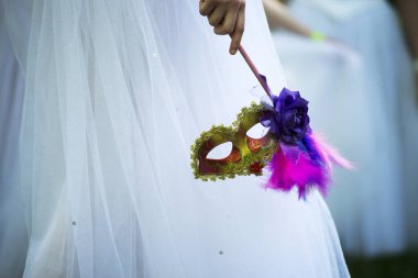 Beyaz elbisenin önünde Venedik karnaval maskesi. Renkli tüyleri olan güzel altın karnaval maskesi. Kadın kostüm ayrıntıları ve lüks retro kıyafetler. Zarif bir tarz. Aptal antika karnavalı.