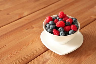 Kırsal ahşap masadaki beyaz kasede olgun, farklı meyveler. Hasat Konsepti. Kırmızı ahududular yakın plan. Sağlıklı, organik gıda ve beslenme konsepti. yemek yemek,