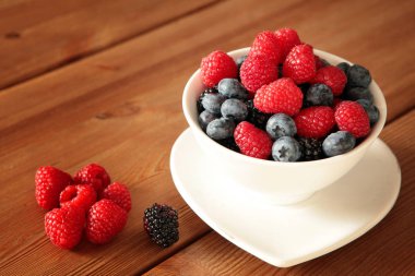 Kırsal ahşap masadaki beyaz kasede olgun, farklı meyveler. Hasat Konsepti. Kırmızı ahududular yakın plan. Sağlıklı, organik gıda ve beslenme konsepti. yemek yemek,