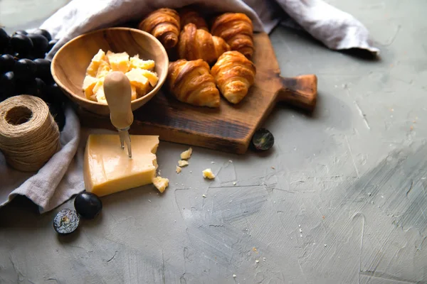 Оригинальные французские круассаны с сыром и виноградом на деревянном столе. Булочка из булочки с булочкой, характерная форма полумесяца. Сыр в миске, нож, разделочная доска в качестве фона . — стоковое фото