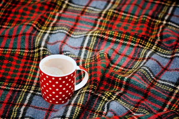 Red dotted teacup with hot chocolate on a Scottish blanket. Cozy home concept with red porcelain mug. A Cup of festive hot chocolate. Traditional homemade Christmas advertising cocoa. New years