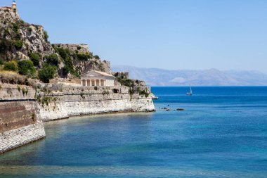 Corfu island Acropolis and boat on the sea. Mountains view. lush green countryside, rugged mountains and idyllic view. Historical building and vacation concept. Ancient alike greek temple