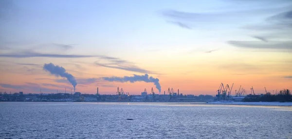 Winter Pink sunset and Urban Landscape view on a Baltic Sea Side. Sunset with snowy boulders and beach landscape. Baltic sea, cold and windy winter time. Smog Pipes and smoke at the factories