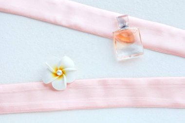 Güzel şişede pembe kadın parfümü ve pembe arka planda beyaz çiçek.