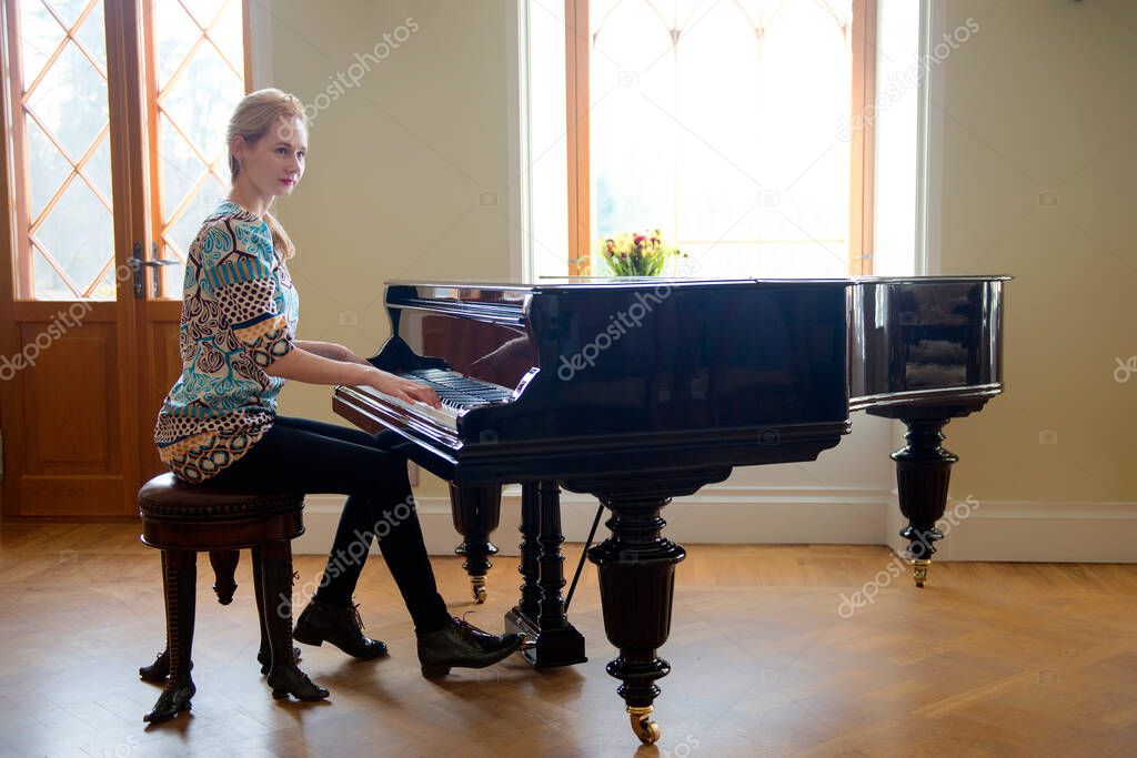 Pianist woman playing forte-piano in front the window at the castle. Women equality and achievements concept