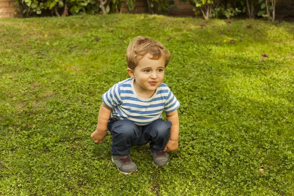 Tiro completo retrato bonito sorridente bebê menino agachamento na grama — Fotografia de Stock